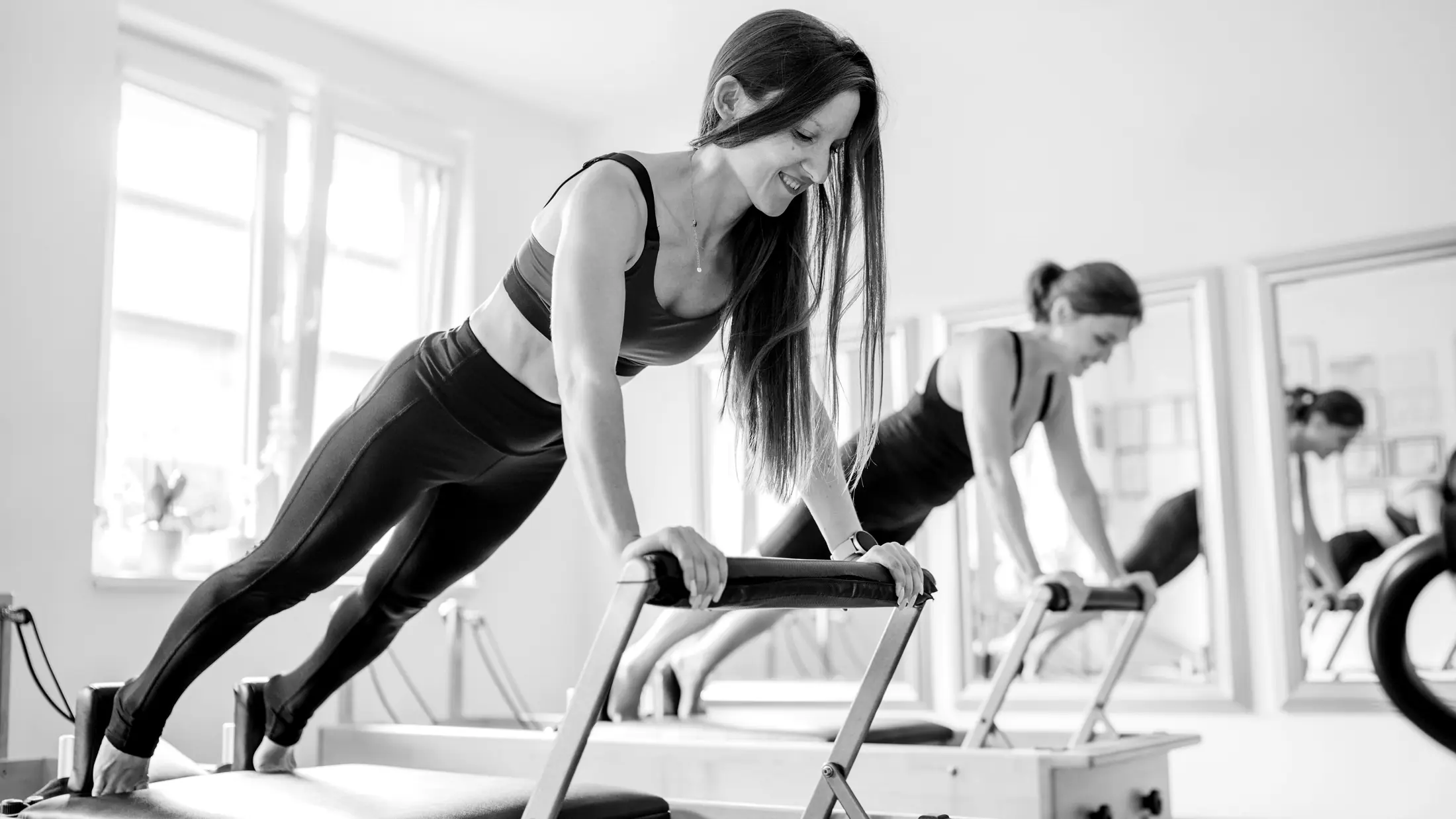 Two women working side by side on Pilates reformers in a bright West Omaha studio